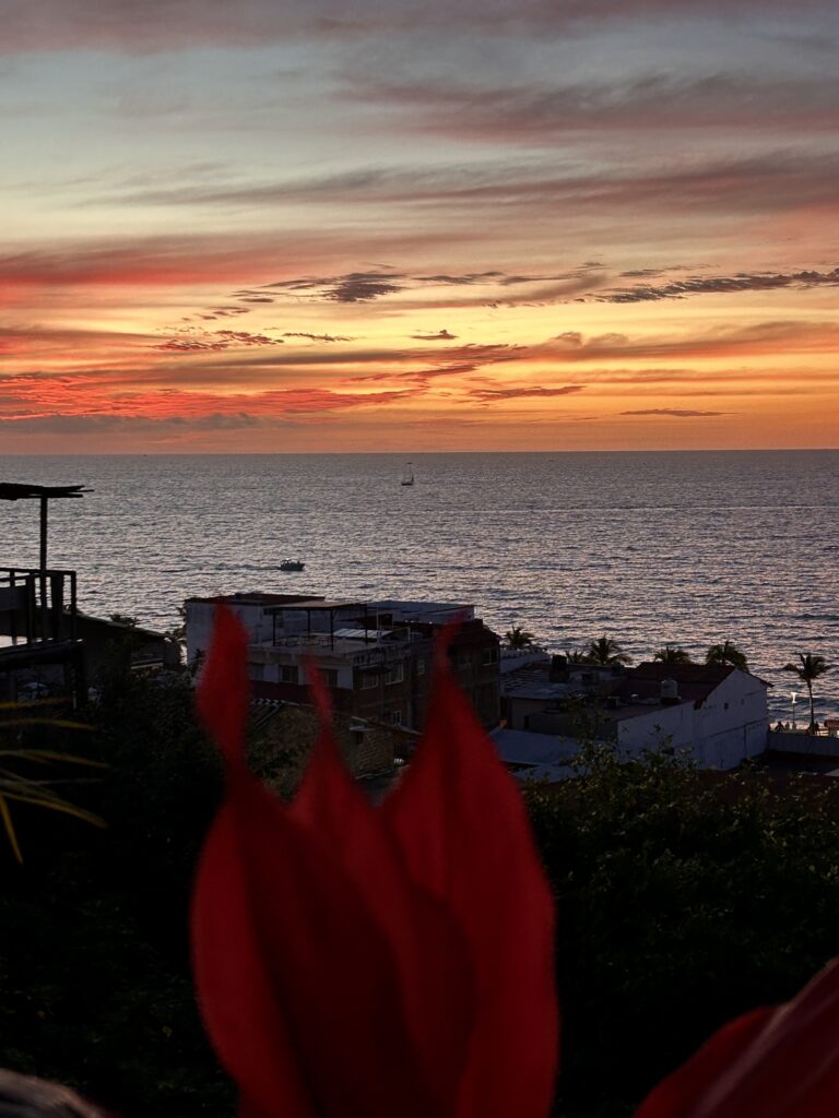 the sun has set and the sky is a burst of orange and yellow and deep purple streaks hovering over a gray ocean.