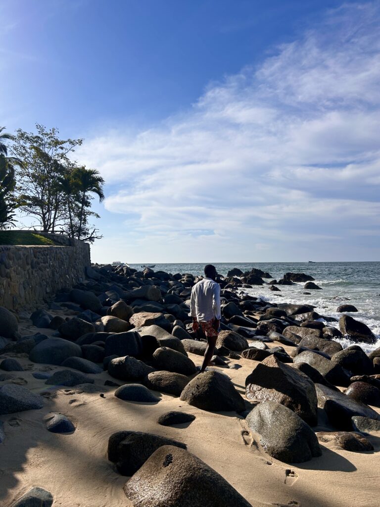 A man walks towards the ocean admist smooth sand and a sea of smooth rocks