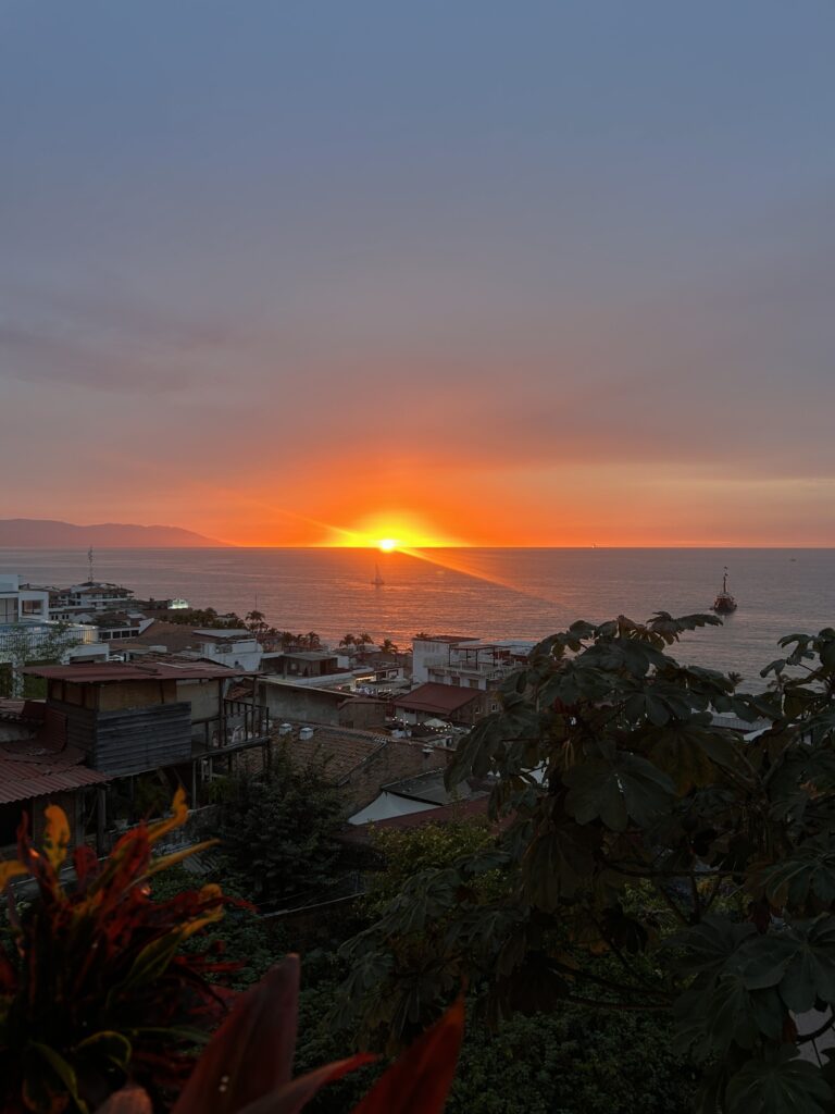 The Sun is a bright fiery orange at the edge of the horizon, over a now gray blue ocean matching the dark gray of the evening sky