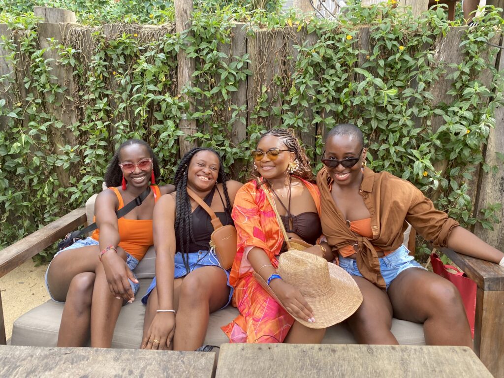 four black women sit close together and smile at the camera. 