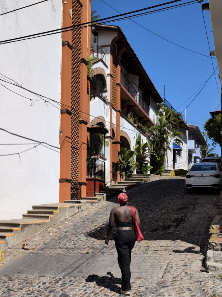 A Black woman in a crop top and low rise pants walks up an incline road in Puerto Vallarta